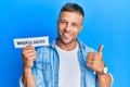 Handsome muscle man holding mindfulness word on paper smiling happy and positive, thumb up doing excellent and approval sign