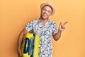 Handsome muscle man holding suitcase going on summer vacation smiling happy pointing with hand and finger to the side Royalty Free Stock Photo