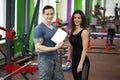 Handsome muscled male trainer consulting attractive young female in gym, both smiling.