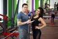 Handsome muscled male trainer consulting attractive young female in gym, both smiling.