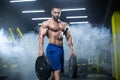 Handsome muscular athlete man is standing in a gym against the background of smoke holding barbell discs in both hands Royalty Free Stock Photo