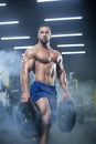 Handsome muscular athlete man is standing in a gym against the background of smoke holding barbell discs in both hands Royalty Free Stock Photo