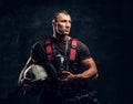 Handsome muscular fireman holding a helmet and oxygen mask standing in the studio against a dark textured wall