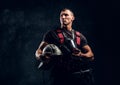 Handsome muscular fireman holding a helmet and oxygen mask standing in the studio against a dark textured wall