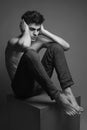 Handsome muscular male model in blue jeans with perfect muscular body posing over wooden background, sitting on a wooden cube and Royalty Free Stock Photo