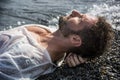 Handsome muscular man on the beach laying on gravel Royalty Free Stock Photo