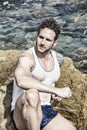 Handsome muscular man on the beach sitting on rocks