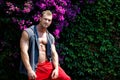 Handsome muscular young man outdoors with flowers behind