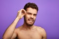 Handsome naked guy plucking his eyebrows, expressing negative emotions. Isolated on blue background