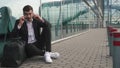 Handsome and nervous businessman in glasses at the airport sitting on the ground with luggage and waiting for his