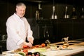 Handsome old cook with grey hair, moustage and beard fixing a meal.