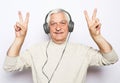 Handsome old man in casual wear and headphones is listening to music using a mobile and smiling Royalty Free Stock Photo