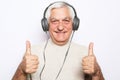 Handsome old man in casual wear and headphones is listening to music on white background Royalty Free Stock Photo
