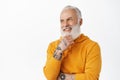 Handsome old man with tattoos, touch his beard thoughtful, smiling and looking satisfied at upper left corner empty Royalty Free Stock Photo