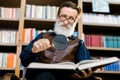 Handsome pensive senior bearded man, librarian or professor, in the library, sitting on the background of bookcases Royalty Free Stock Photo