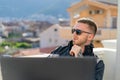 Handsome pensive stylish man sitting on balcony and working on laptop Royalty Free Stock Photo