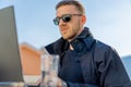 Handsome pensive stylish man sitting on balcony and working on laptop Royalty Free Stock Photo