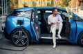 Handsome person with smartphone. Man with blue electric car on the charge station