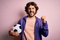 Handsome player man with beard playing soccer holding football ball over pink background screaming proud and celebrating victory Royalty Free Stock Photo