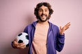 Handsome player man with beard playing soccer holding football ball over pink background very happy and excited, winner expression Royalty Free Stock Photo