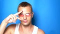 Handsome playful guy in pink glasses on a blue background, dancing and making funny faces. portrait. copy space