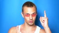 Handsome playful guy in pink glasses on a blue background, dancing and making funny faces. portrait. copy space