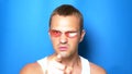 Handsome playful guy in pink glasses on a blue background, dancing and making funny faces. portrait. copy space