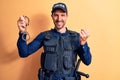 Handsome policeman wearing uniform and bulletprof holding handcuffs over yellow background screaming proud, celebrating victory