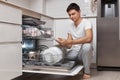 handsome positive man putting plates in dishwasher machine Royalty Free Stock Photo