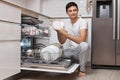 handsome positive man putting plates in dishwasher machine Royalty Free Stock Photo