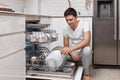 handsome positive man putting plates in dishwasher machine Royalty Free Stock Photo