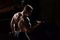 Handsome power athletic guy bodybuilder doing exercises with dumbbell. Fitness muscular body on dark background. Royalty Free Stock Photo