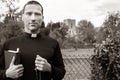 Good looking priest stands in front of fence to field with church in background Royalty Free Stock Photo