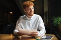 Handsome readhead bearded man sitting at wooden table, holding p