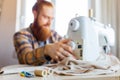 handsome redhaired man with long beard sews at a sewing machine at home studio