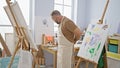 Handsome, relaxed young man artist concentrating intently while drawing, standing wearing apron indoors at his artsy university