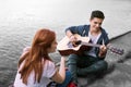 Handsome romantic boyfriend playing the guitar for his girlfriend sitting near river