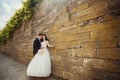 Handsome romantic groom kissing beautiful brunette bride near old wall castle