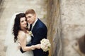 Handsome romantic groom kissing beautiful brunette bride near old wall castle