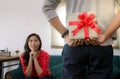 Handsome romantic man hiding a gift box behind his back surprising his girlfriend on special day