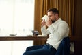 Handsome self-confident European businessman, entrepreneur on business trip drinking coffee, sitting at a desk in hotel room