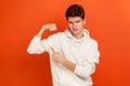 Handsome self confident teenager in casual style sweatshirt pointing finger on his arm muscle, pumping in gym, discount