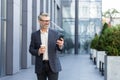 A handsome senior businessman is standing outside an office center with a cup of coffee and using the phone Royalty Free Stock Photo