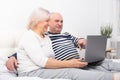 Handsome senior couple woman and man sitting in bed using laptop at home Royalty Free Stock Photo