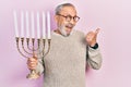 Handsome senior man with beard holding menorah hanukkah jewish candle pointing thumb up to the side smiling happy with open mouth Royalty Free Stock Photo