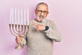 Handsome senior man with beard holding menorah hanukkah jewish candle smiling happy pointing with hand and finger Royalty Free Stock Photo