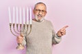 Handsome senior man with beard holding menorah hanukkah jewish candle smiling happy pointing with hand and finger to the side Royalty Free Stock Photo