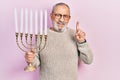 Handsome senior man with beard holding menorah hanukkah jewish candle smiling with an idea or question pointing finger with happy Royalty Free Stock Photo