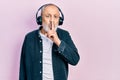 Handsome senior man with beard listening to music using headphones asking to be quiet with finger on lips Royalty Free Stock Photo