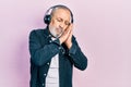 Handsome senior man with beard listening to music using headphones sleeping tired dreaming and posing with hands together while Royalty Free Stock Photo